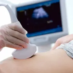 Pierwsze usg ciąży. Dłoń w rękawiczce trzyma sondę aparatu USG, która przesuwa się po brzuchu kobiety. Na ekranie widoczny obraz.