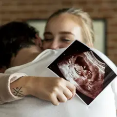 Szczęśliwa para przytula się, trzymając zdjęcie USG. To idealny moment, kiedy powiedzieć rodzinie o ciąży.
