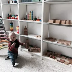 Małe dziecko w bawialni Montessori, otoczone drewnianymi zabawkami edukacyjnymi, takimi jak tęczowe łuki i klocki.