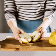 Ręce trzymają połówki gruszki, obok leżą całe. Idealne owoce dla 8 miesięcznego dziecka, łatwe do przygotowania.