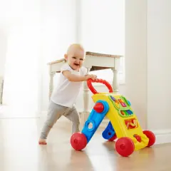 Uśmiechnięte dziecko uczy się chodzić z kolorowym pchaczem, polecanym przez fizjoterapeutów.