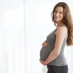 Uśmiechnięta ciężarna kobieta trzymająca się za brzuch, czując delikatne ciągnięcie brzucha w ciąży podczas chodzenia.