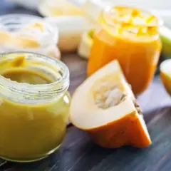 Słoiczki z puree warzywnym i kawałki dyni oraz jabłka na drewnianym tle.