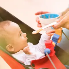 Karmienie 4-miesięcznego niemowlęcia. Zastanawiasz się, ile powinno jeść 4 miesięczne niemowlę? Maluch w leżaczku z zaciekawieniem patrzy na łyżeczkę z jedzeniem.