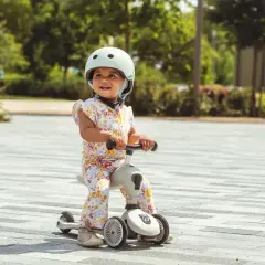 Uśmiechnięte dziecko w kasku na jeździku. Fizjoterapeuta poleca scoot and ride dla rozwoju malucha.