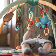 Rączki 11-miesięcznego dziecka sięgają do kolorowych zabawek na macie edukacyjnej. Radość i odkrywanie świata podczas zabawy.