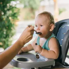 Maluch w krzesełku do karmienia z zaciekawieniem przyjmuje pierwszy posiłek. To ważny moment, kiedy rozszerzać dietę dziecka karmionego piersią.