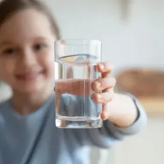 Uśmiechnięta dziewczynka podaje szklankę czystej wody. To doskonały wybór, jaka woda dla rocznego dziecka.