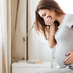 Kobieta w ciąży czuje poranne mdłości, trzymając się za usta.