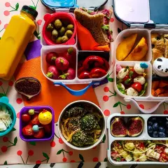 Kolorowy lunchbox z owocami, warzywami, kanapką i napojem.