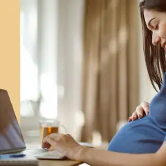 Ciężarna kobieta pracuje przy laptopie, czując ruchy dziecka. Ułożenie główkowe i aktywność malucha są widoczne.