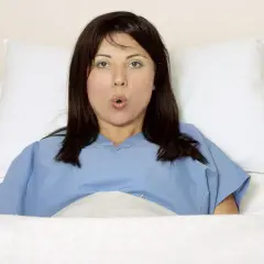 Kobieta w niebieskiej koszuli szpitalnej, w 38 tygodniu ciąży, leży w łóżku z poduszkami.