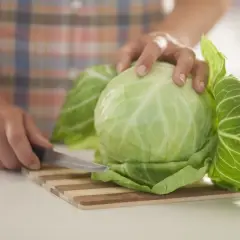 Ręce kroją świeżą kapustę na desce. Zielona kapusta na piersi, gotowa do przygotowania pysznego posiłku.