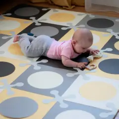 Dziecko bawi się na macie Skip Hop, która jest już wycofana. Zabawki i kolorowa mata tworzą radosną atmosferę.