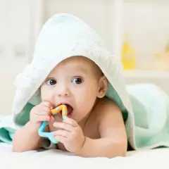Maluch w miętowym kocyku z gryzakiem w buzi, jakby wyciągał rączki do rodziców.