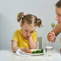 Mama zachęca dziecko do jedzenia brokułów. Trudna dieta dwulatka, ale mama się nie poddaje.