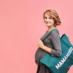 Przyszła mama z torbą "Mamahood" na ramieniu, gotowa do porodu.