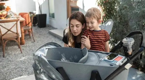 Mama i synek pochylają się nad gondolą spacerówki, jakby zastanawiali się, od kiedy spacerówka będzie im potrzebna.