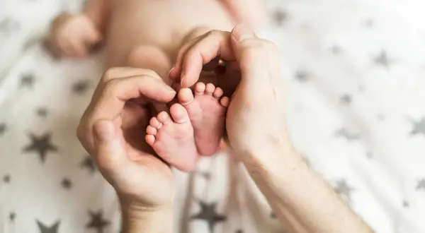 Dłonie otaczają maleńkie stópki 7 tygodniowego dziecka. Delikatne paluszki i pięty są objęte czułością.