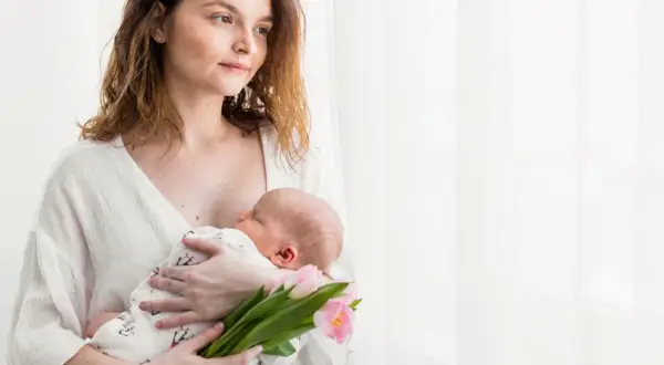 Mama tuli z dzieckiem na rękach, trzymając bukiet różowych tulipanów. To piękny obrazek z 4 trymestru.