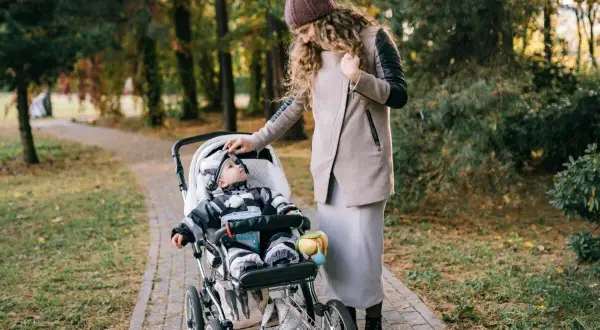 Mama poprawia czapkę malucha, który siedzi w spacerówce. Jesienny spacer po parku.