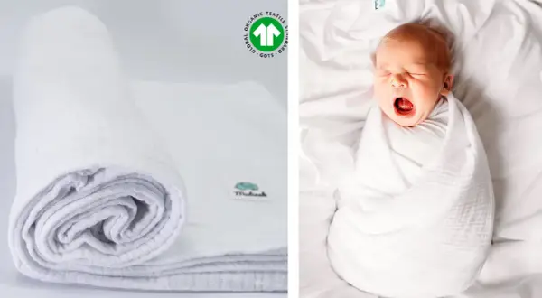 Biały, zwinięty otulacz muślinowy obok śpiącego niemowlaka. Certyfikat GOTS potwierdza jego ekologiczne pochodzenie.
