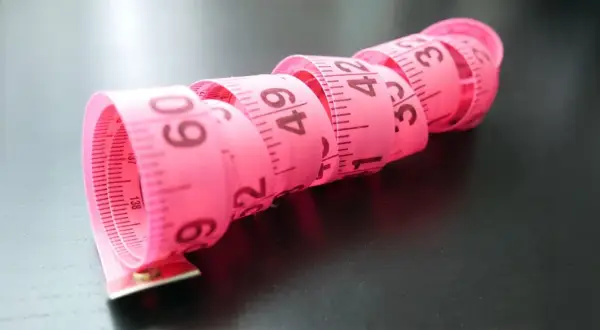 Różowa miarka krawiecka zwinięta w spirale, z widocznymi centymetrami. Idealna do określenia rozmiaru buta 2 latka.
