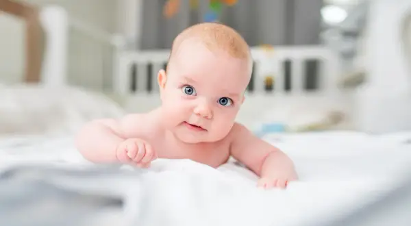 Niebieskooki, 3-miesięczny maluch leży na brzuchu, ćwicząc mięśnie szyi.