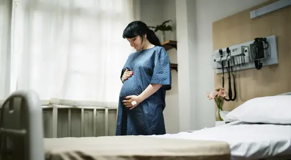Kobieta w szpitalnej sali, trzymająca się za brzuch, szuka sposobów, jak złagodzić skurcze porodowe.
