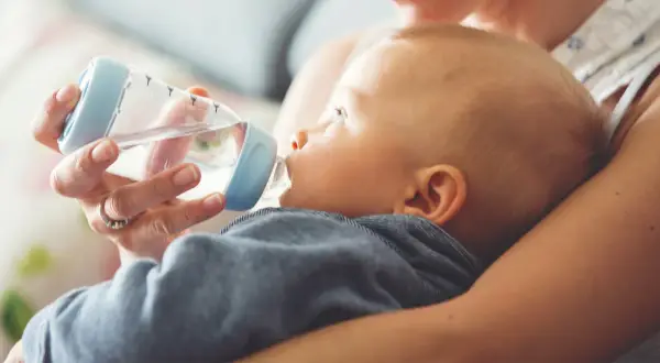 Mama próbuje nakarmić butelką dziecko, które nie chce pić wody.