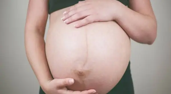 Brzuch kobiety w ciąży, dłonie delikatnie go obejmują. To czas, gdy czuć już wyraźne ruchy dziecka w 27 tygodniu ciąży.