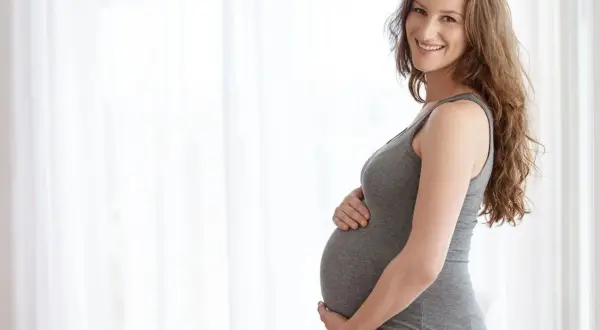 Uśmiechnięta ciężarna kobieta trzymająca się za brzuch, czując delikatne ciągnięcie brzucha w ciąży podczas chodzenia.