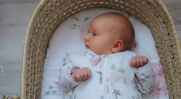 Malutkie dziecko w śpiworku z motywem kwiatowym, leżące w wiklinowym koszu. Od kiedy kołderka dla niemowlaka jest tak urocza?
