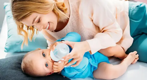 Uśmiechnięta mama karmi butelką dziecko. Ile powinno trwać karmienie butelką? To zależy od malucha.