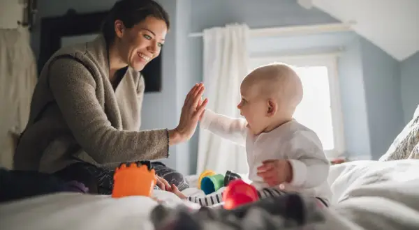 Radosne zabawy z 10 miesięcznym dzieckiem na łóżku. Mama i maluch dają sobie "piątkę".