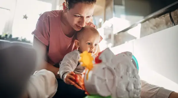 Mama bawi się z 5-miesięcznym dzieckiem, które z zaciekawieniem ogląda kolorową zabawkę.