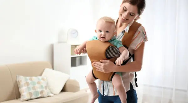 Uśmiechnięta mama trzyma dziecko w wygodnym nosidle. To alternatywa dla chusty, zapewniająca komfort i bezpieczeństwo.