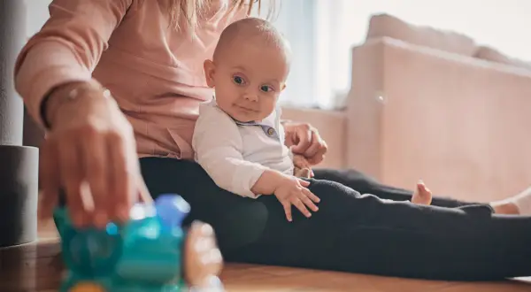 Mama bawi się z 9-miesięcznym dzieckiem, które siedzi na jej kolanach. Przed nimi leży zabawkowy pociąg, idealny do zabawy dla malucha.
