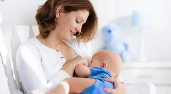 Uśmiechnięta mama karmi piersią dziecko w bujanym fotelu. Dobra dieta przy karmieniu piersią to podstawa.