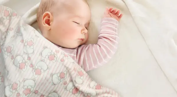 Śpiące dziecko otulone kocykiem w misie. Idealne wymiary kocyka dla niemowlaka zapewnią komfortowy sen.