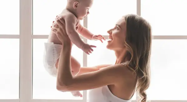 Szczęśliwa mama podrzuca w górę swoje 7 miesięczne dziecko.