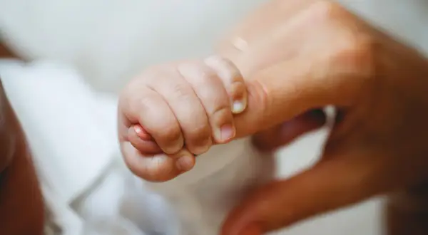 Dłoń noworodka mocno ściska palec dorosłego. To piękny przykład odruchów noworodkowych, instynktownej więzi.