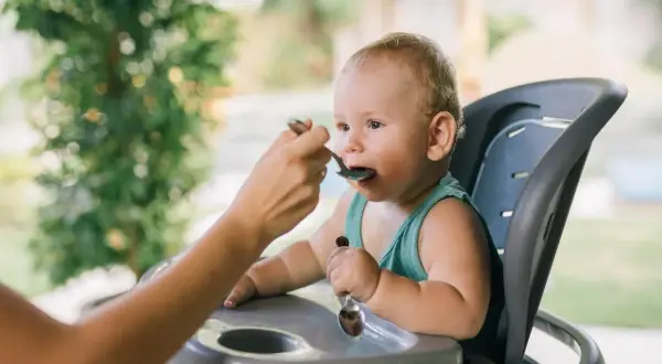 Maluch w krzesełku do karmienia z zaciekawieniem przyjmuje pierwszy posiłek. To ważny moment, kiedy rozszerzać dietę dziecka karmionego piersią.