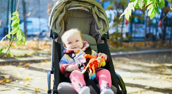 Uśmiechnięte dziecko w wózku spacerowym, idealnym do jakiego wieku, bawi się kolorową zabawką.