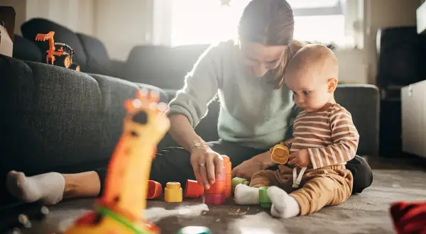Mama i 7-miesięczne dziecko bawią się kolorowymi klockami na dywanie. Radość i nauka przez zabawę.