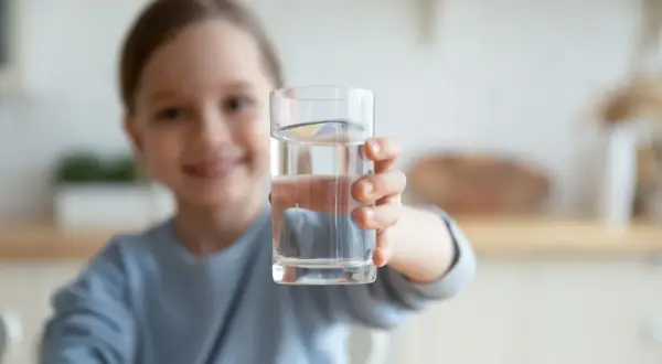Uśmiechnięta dziewczynka podaje szklankę czystej wody. To doskonały wybór, jaka woda dla rocznego dziecka.