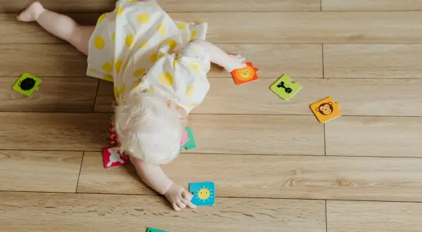 Dziecko z jasnymi włosami leży na podłodze, bawiąc się puzzlami. To etap rozwoju, kiedy dziecko powinno się obracać.