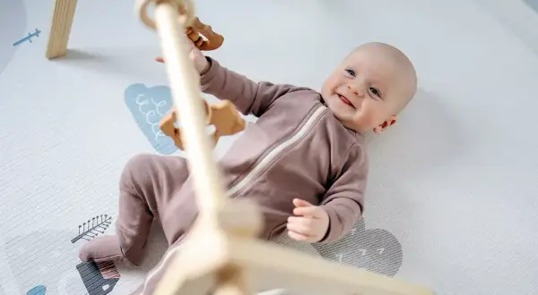 Uśmiechnięte niemowlę bawi się na macie edukacyjnej. Od kiedy niemowlę może korzystać z takiej maty? Od pierwszych dni życia!