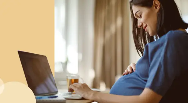 Ciężarna kobieta pracuje przy laptopie, czując ruchy dziecka. Ułożenie główkowe i aktywność malucha są widoczne.