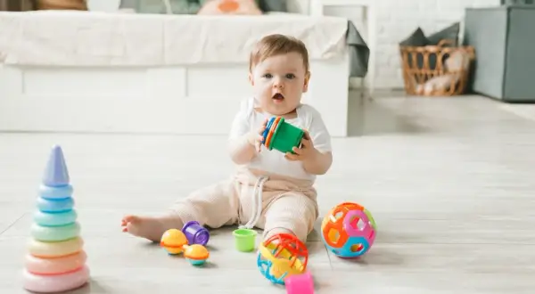 Maluch bawi się kolorowymi zabawkami, które świetnie nadają się na zabawy sensoryczne dla 10-miesięcznego dziecka.